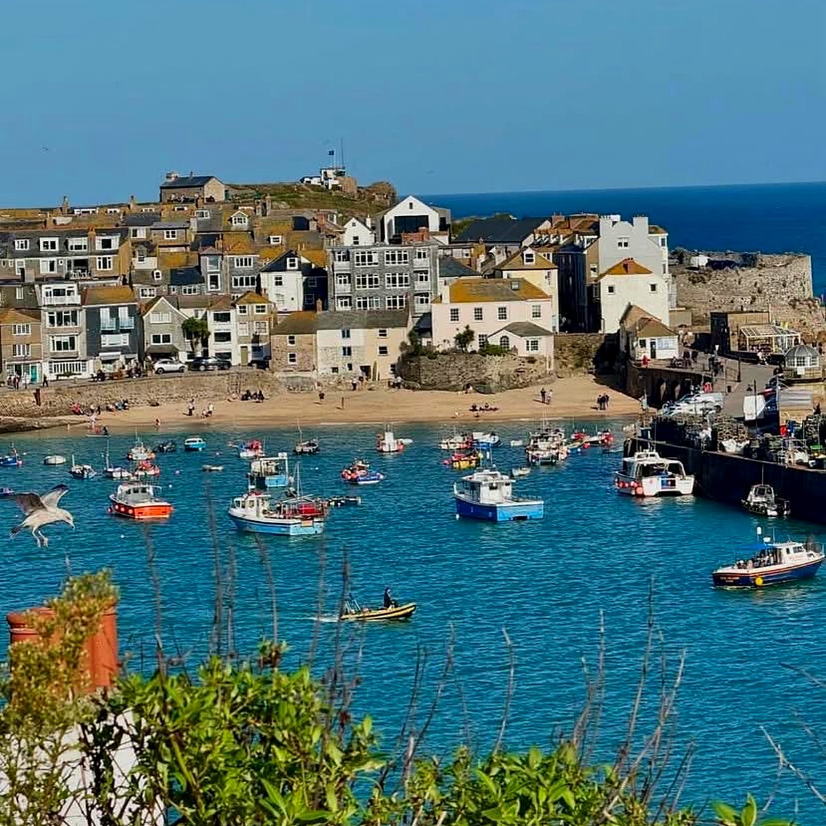St Ives harbour on a sunny day, with boats on turquoise water, the sandy beach and the town behind